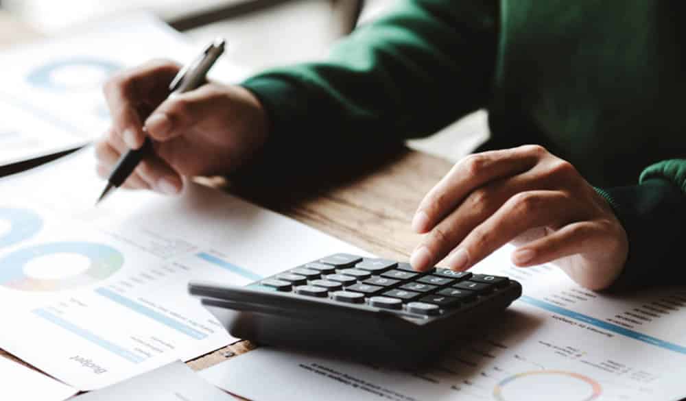 Bank auditor reviewing documents on a desk using a calculator.