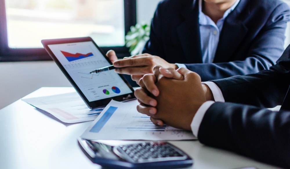 CPA and business man investor talking about employee benefit plans chart information in mobile tablet together sitting in meeting room at office